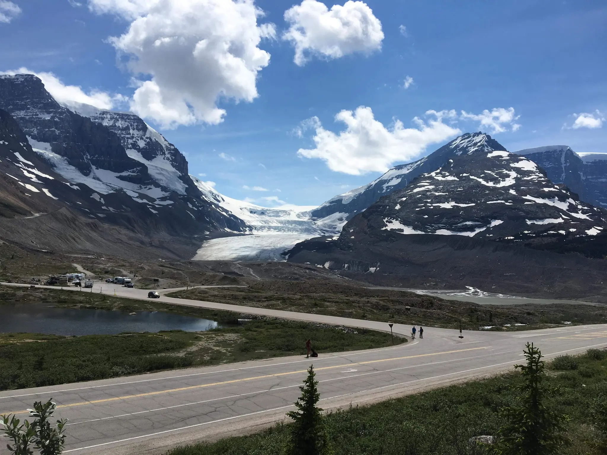road winding through mountains with glacier and small lake